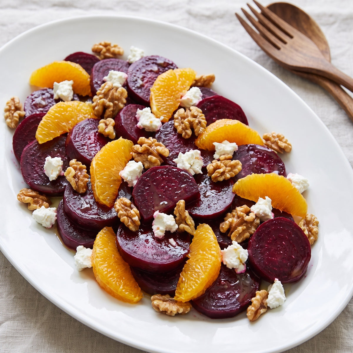 Salade de betteraves marinées avec segments d'orange, fromage de chèvre et morceaux de noix sur un grand plat blanc