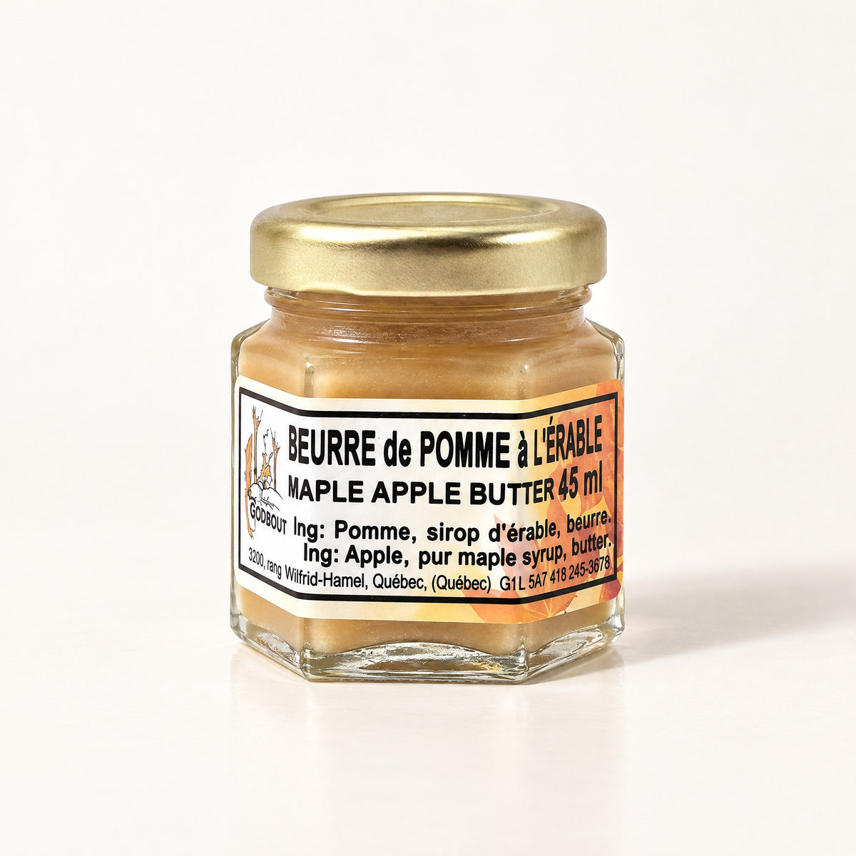Un petit pot de verre hexagonal de beurre de pomme à l'érable avec couvercle doré sur fond crème neutre