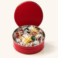 Boîte à bonbons ronde et rouge ouverte, remplie de friandises emballées individuellement sur un fond crème
