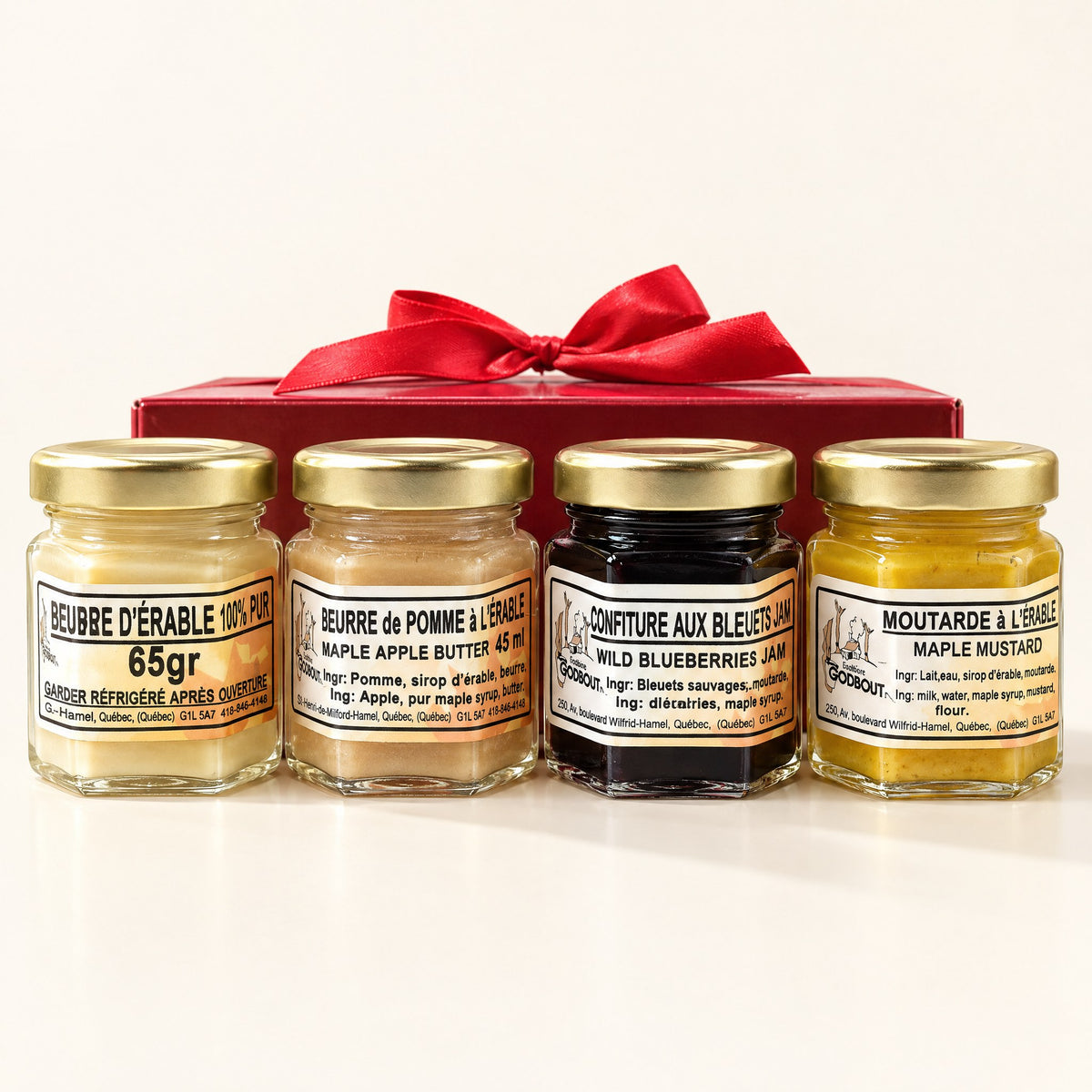 Quatre petits pots de la boîte découverte alignés devant un coffret cadeau rouge sur un fond crème