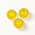Trois bonbons au miel et citron translucides en forme de fleurs jaunes à motif d'abeille sur fond crème