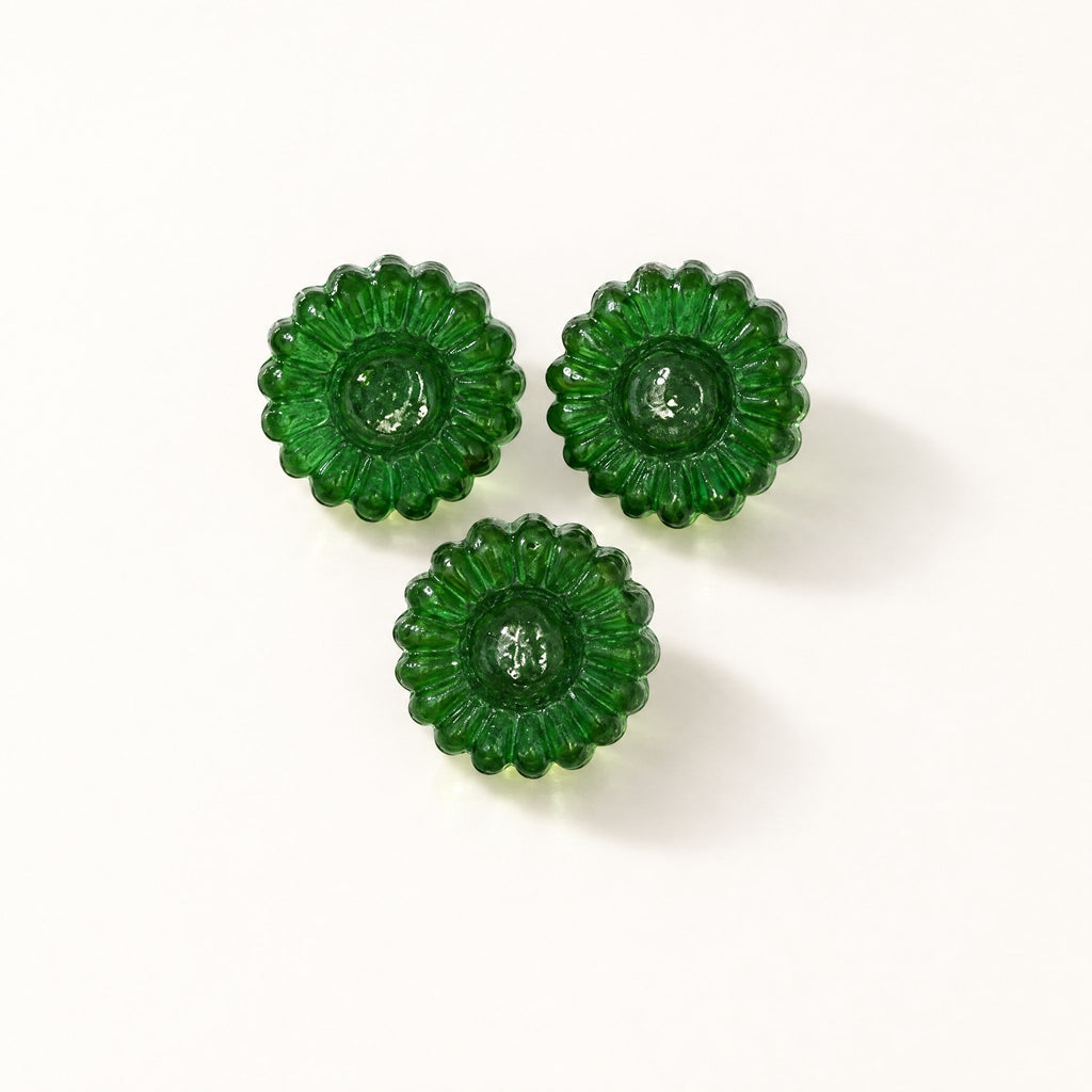 Trois bonbons au miel et eucalyptus verts en forme de fleur, disposés sur un fond crème uni