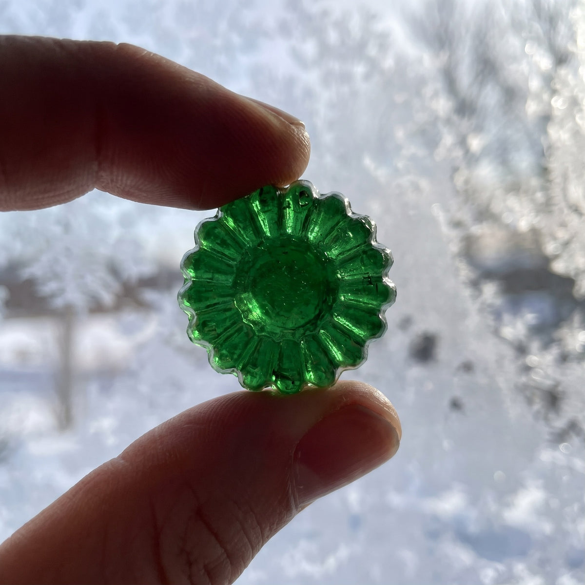 Un bonbon au miel et eucalyptus vert et translucide tenu entre deux doigts devant une fenêtre givrée