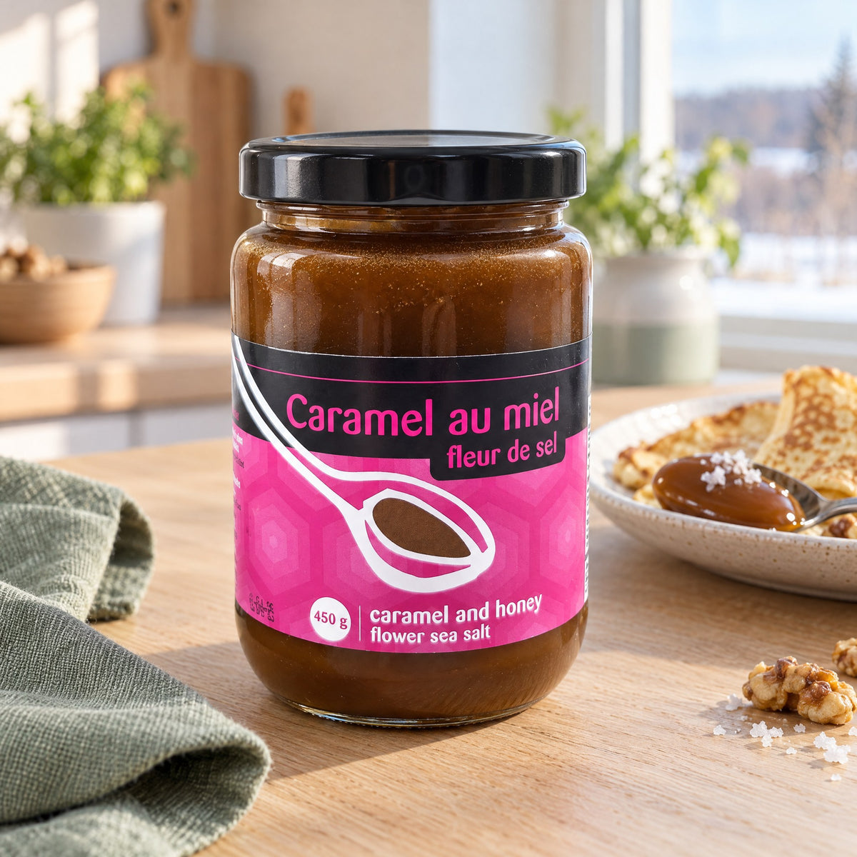 Pot de caramel au miel et fleur de sel posé sur une table en bois, à côté d'une assiette de crêpes