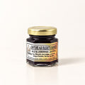 Petit pot hexagonal de confiture aux bleuets sauvages au couvercle doré, présenté sur fond crème uni
