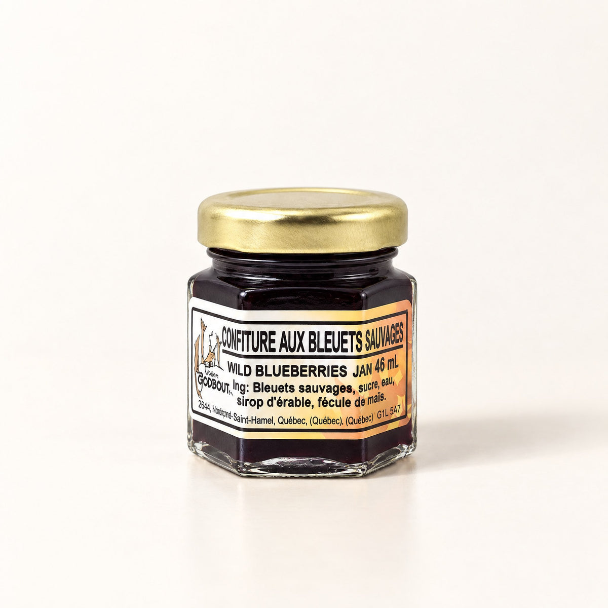 Petit pot hexagonal de confiture aux bleuets sauvages au couvercle doré, présenté sur fond crème uni