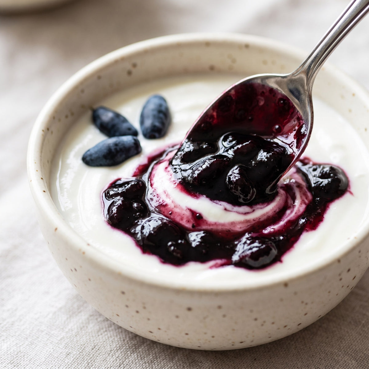 Onctueuse confiture de camerises mélangée à du yogourt blanc dans un bol moucheté avec une cuillère