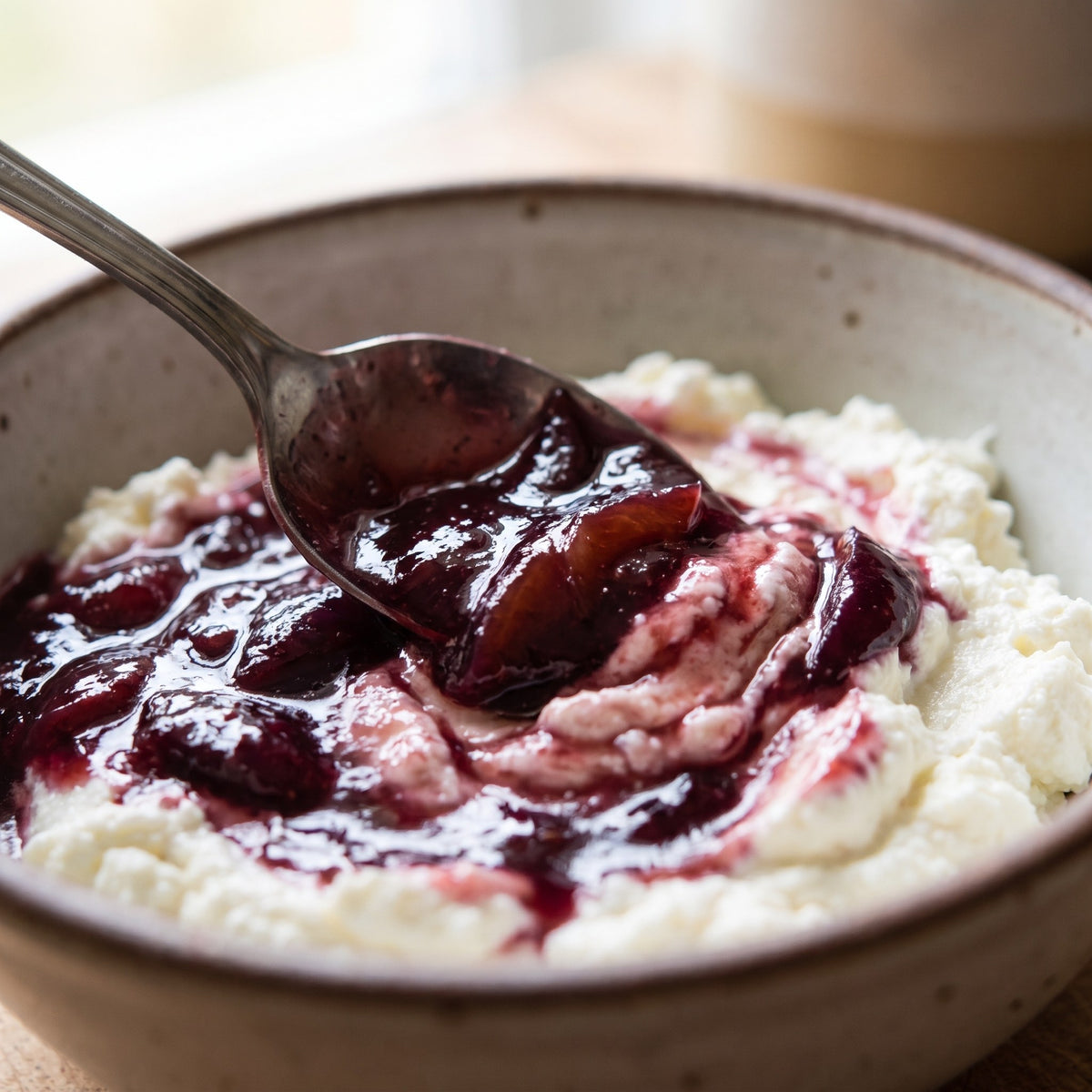 Confiture de prunes violacée servie à la cuillère sur un bol de fromage frais onctueux