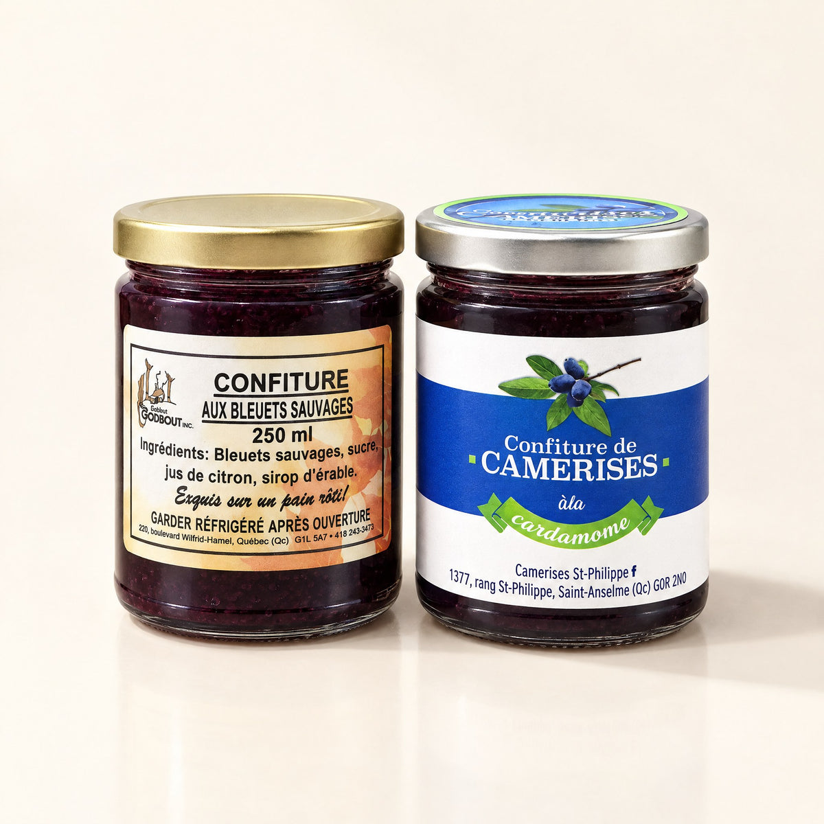 Un duo de confitures — bleuets & camerises présenté dans deux pots en verre côte à côte sur un fond beige crème