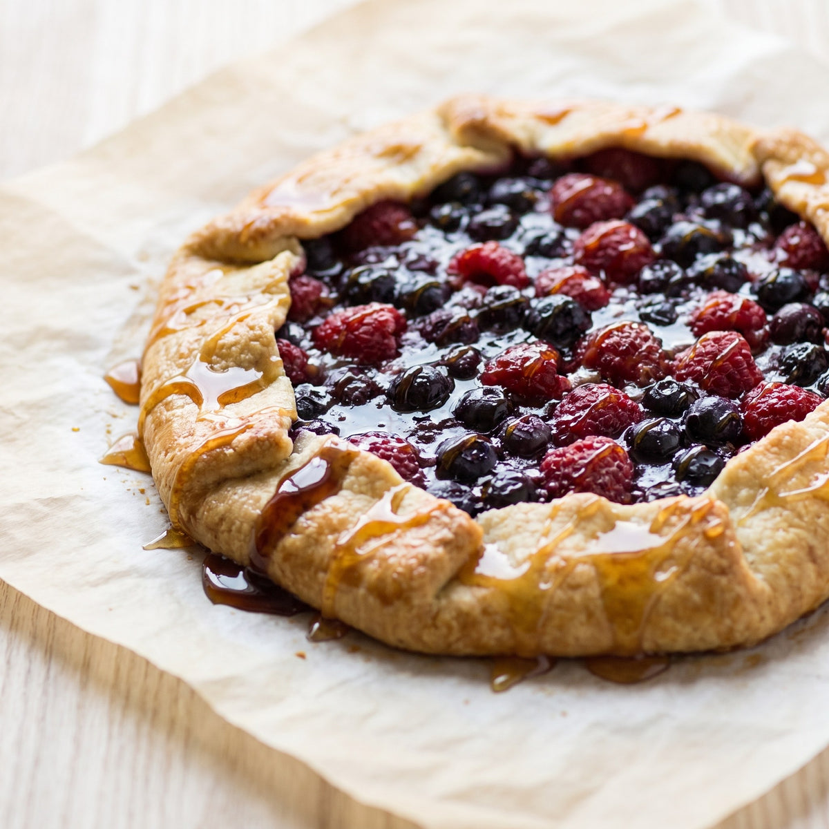 Tarte rustique aux bleuets et framboises arrosée du Duo de miel fruitier sur du papier parchemin