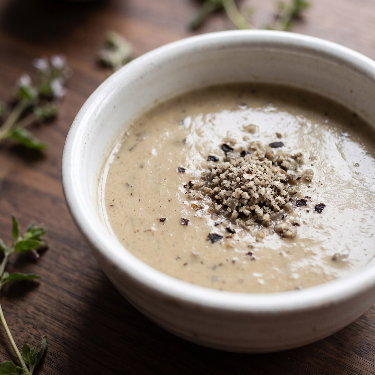 Un bol de potage crémeux garni de duo de sel aux champignons, posé sur une table en bois avec de petites herbes