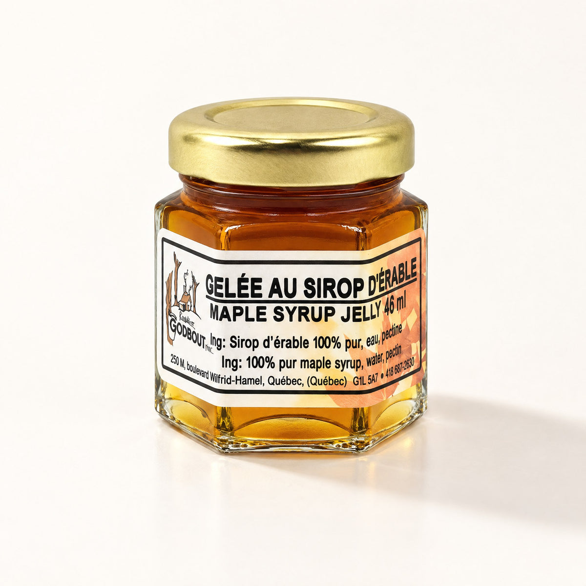 Un petit pot hexagonal de gelée au sirop d'érable fermé par un couvercle doré, posé sur un fond crème lumineux