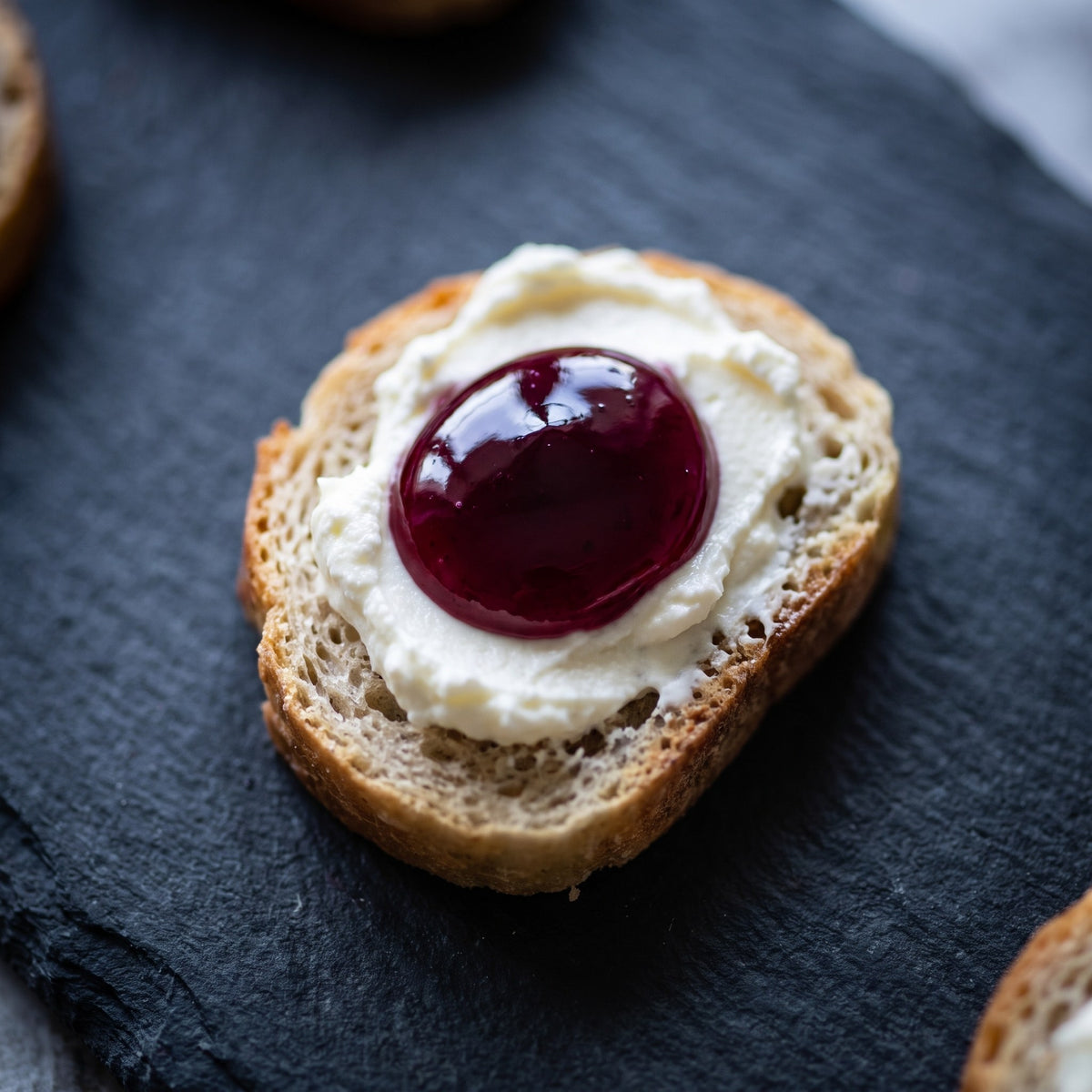 Bouchée de pain grillé garnie de fromage à la crème et d'une brillante gelée de camerises sur une ardoise noire
