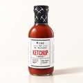 Une bouteille de ketchup épicé du Bas-Saint-Laurent avec étiquette blanche, déposée sur un fond crème uni