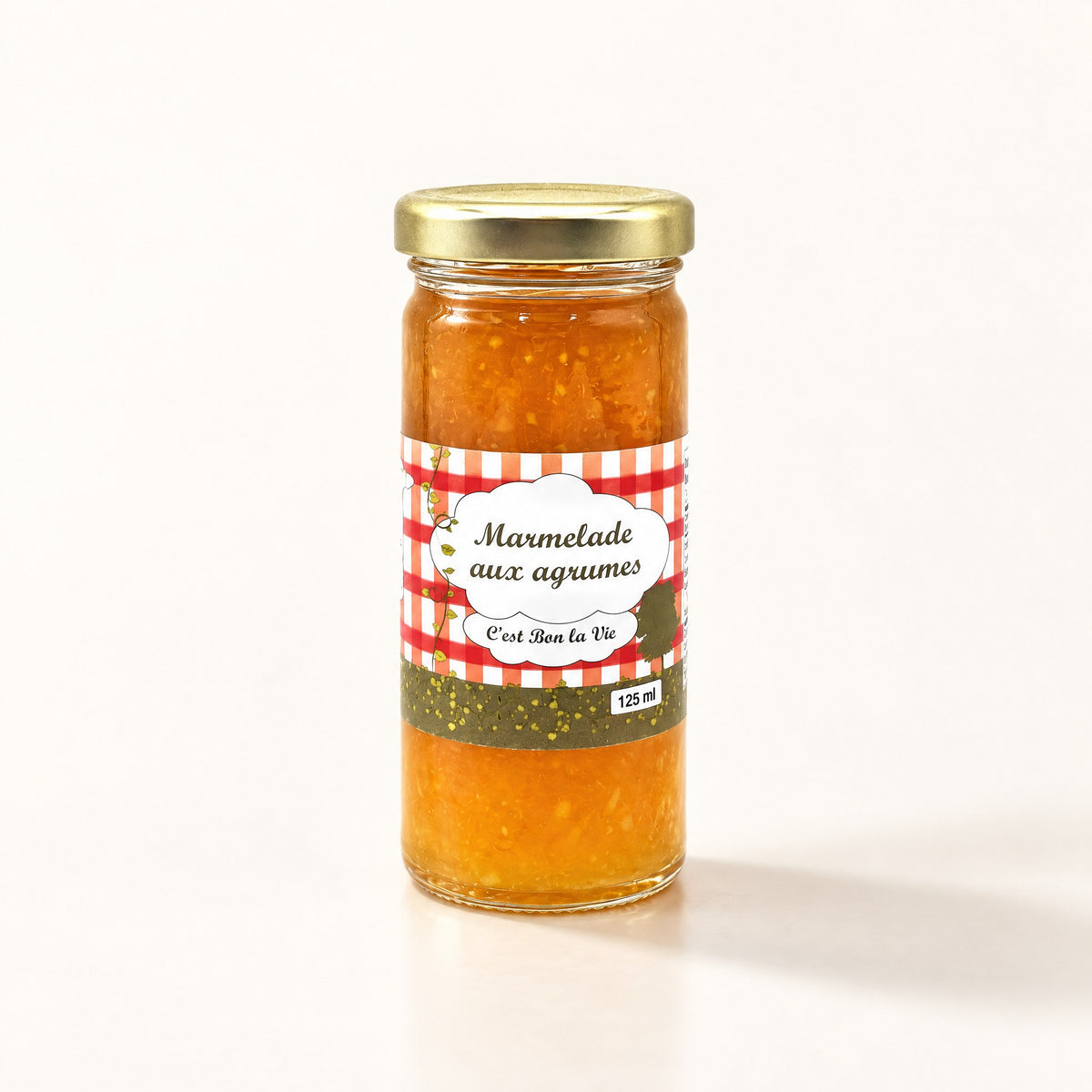 Un pot de marmelade aux agrumes sur fond crème avec son couvercle doré et son étiquette quadrillée rouge