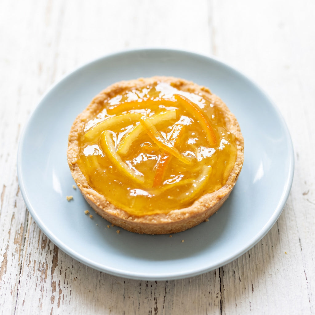 Tartelette garnie de marmelade citrons et oranges sur une assiette bleue, déposée sur une table en bois blanc vieilli