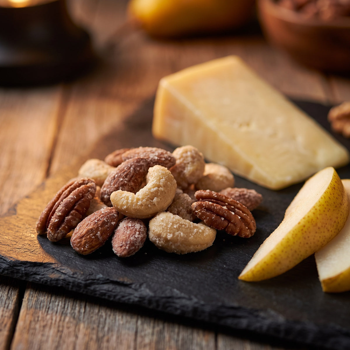 Noix au sucre d'érable croustillantes présentées sur une ardoise à côté d'un bloc de fromage et de tranches de poire