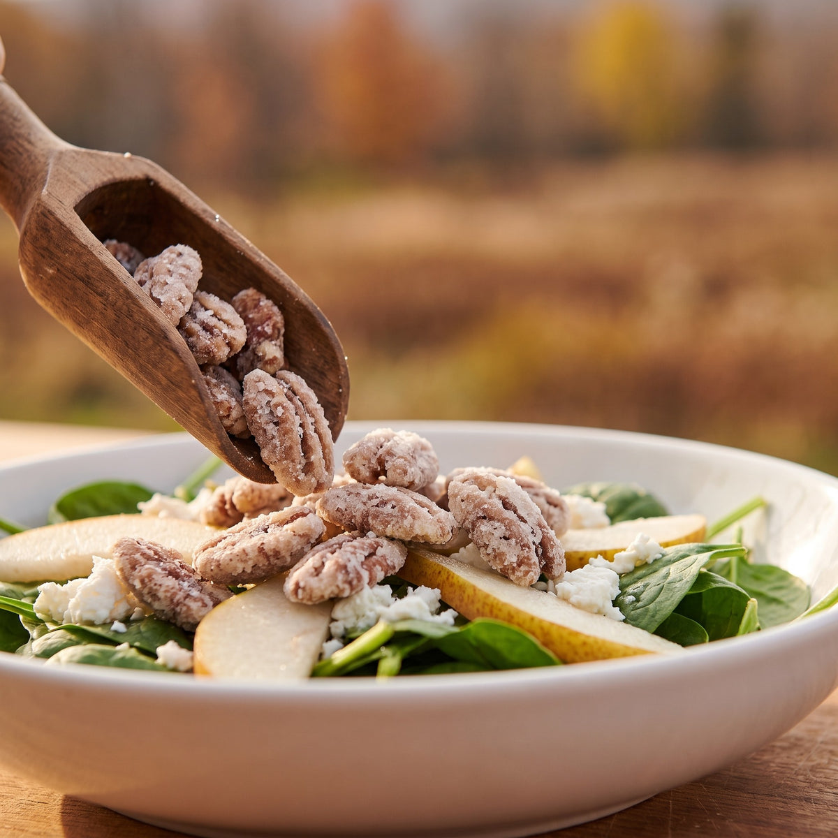 Cuillère de bois versant des pacanes au sucre d'érable sur une salade de poires et épinards avec fond d'automne flou