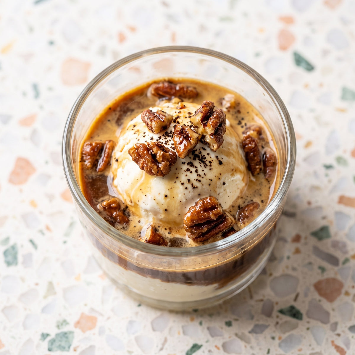 Boule de crème glacée arrosée d'espresso dans un verre, garnie de pacanes Érable et Café, sur une table de terrazzo