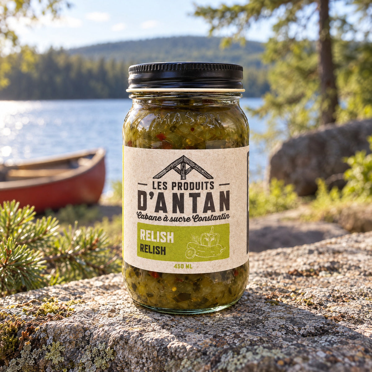 Pot de relish Les Produits d’Antan posé sur une roche au bord d’un lac, avec canot et forêt en arrière-plan