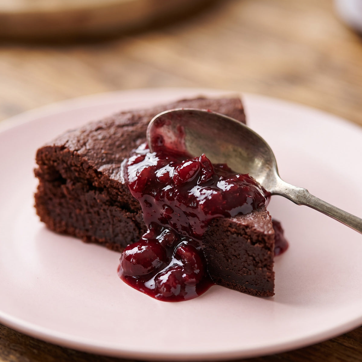 Tartinade de griottes en brisures déposée sur une pointe de gâteau au chocolat dans une assiette rose