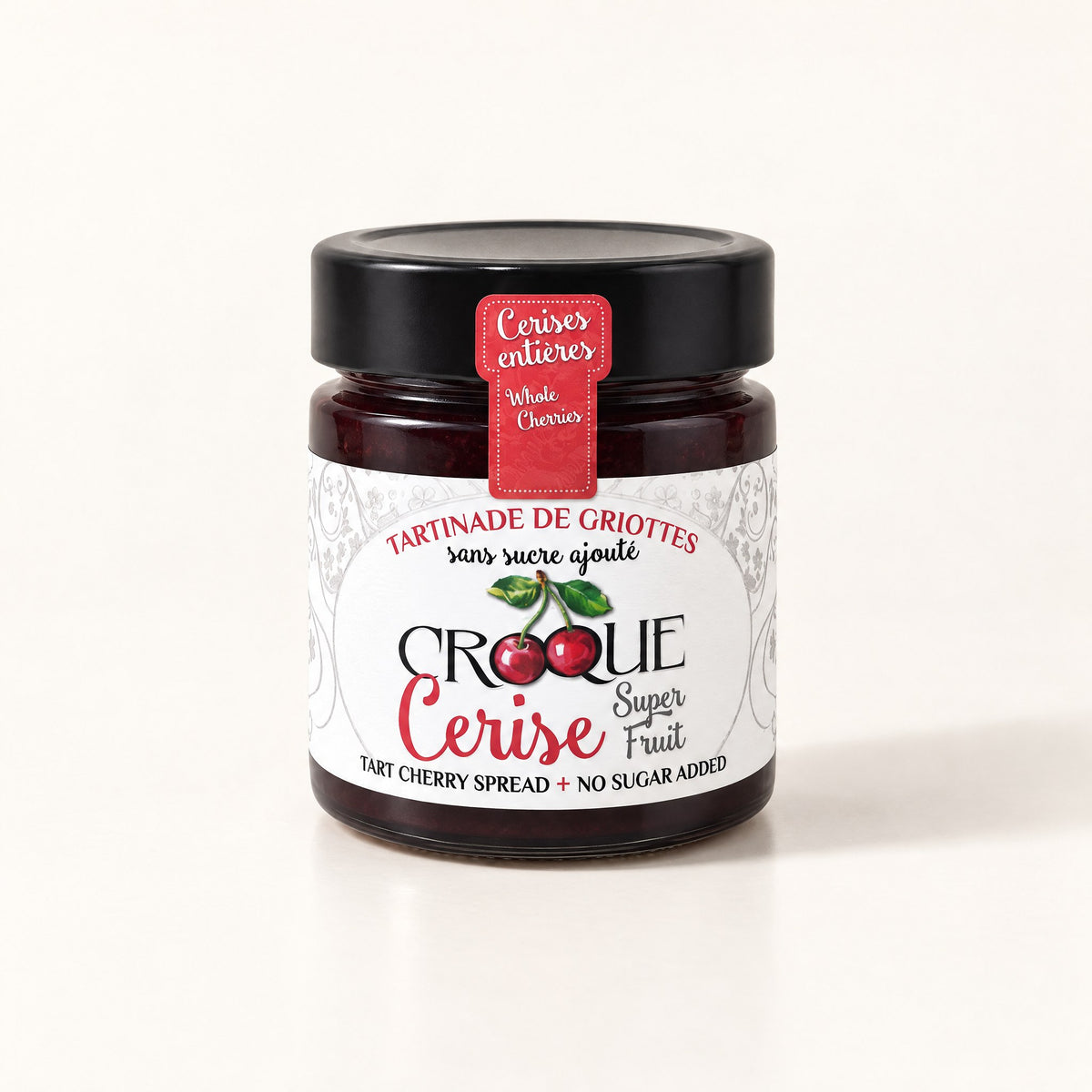 Un pot de verre de tartinade de griottes Croque Cerise avec un couvercle noir, posé sur un fond crème uniforme
