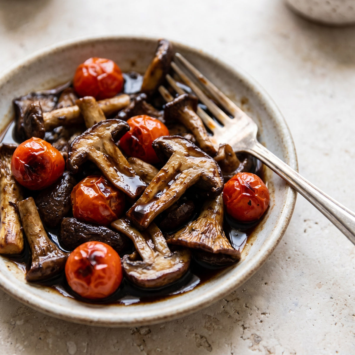 Vinaigre à l’ail noir sur champignons sautés et tomates cerises dans une assiette rustique, avec fourchette