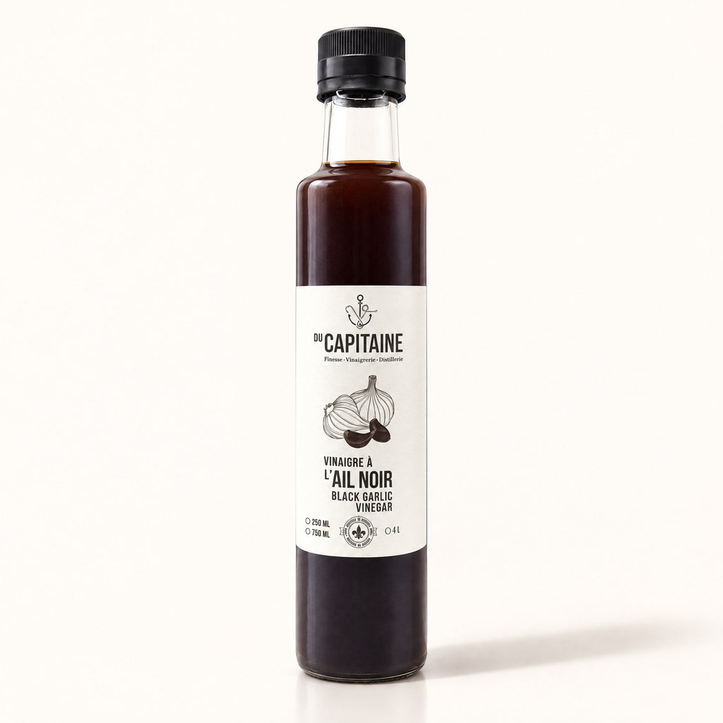 Bouteille de vinaigre à l’ail noir Du Capitaine debout sur fond crème, étiquette blanche visible