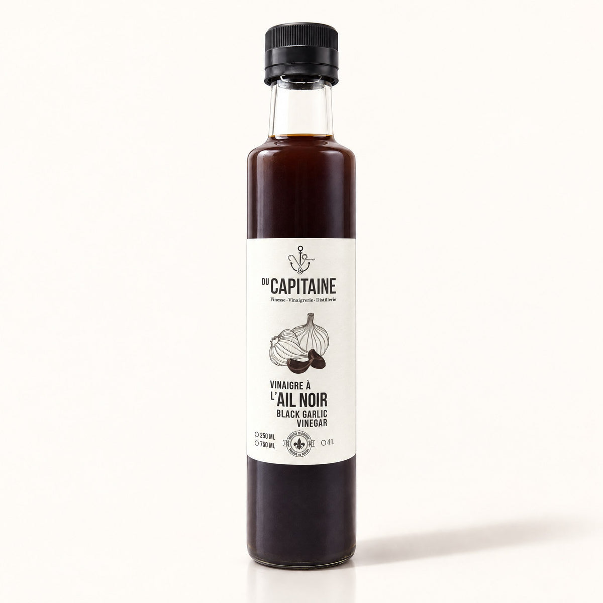 Bouteille de vinaigre à l’ail noir Du Capitaine debout sur fond crème, étiquette blanche visible