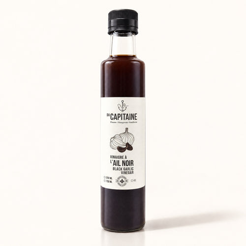 Bouteille de vinaigre à l’ail noir Du Capitaine debout sur fond crème, étiquette blanche visible