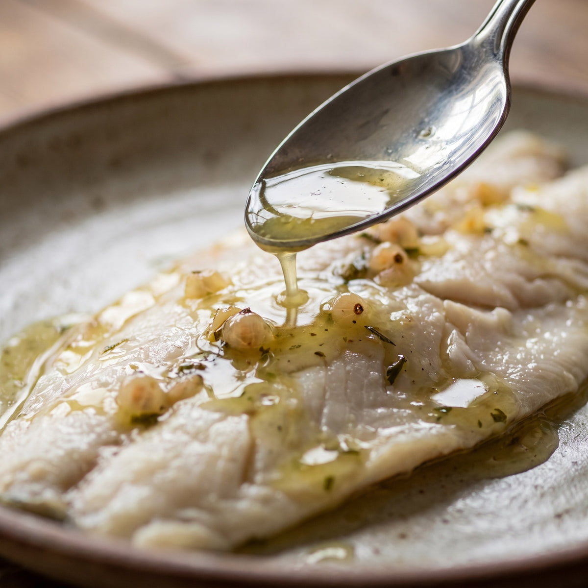 Vinaigre gadelle blanche versé sur un filet de poisson blanc dans une assiette rustique, en gros plan