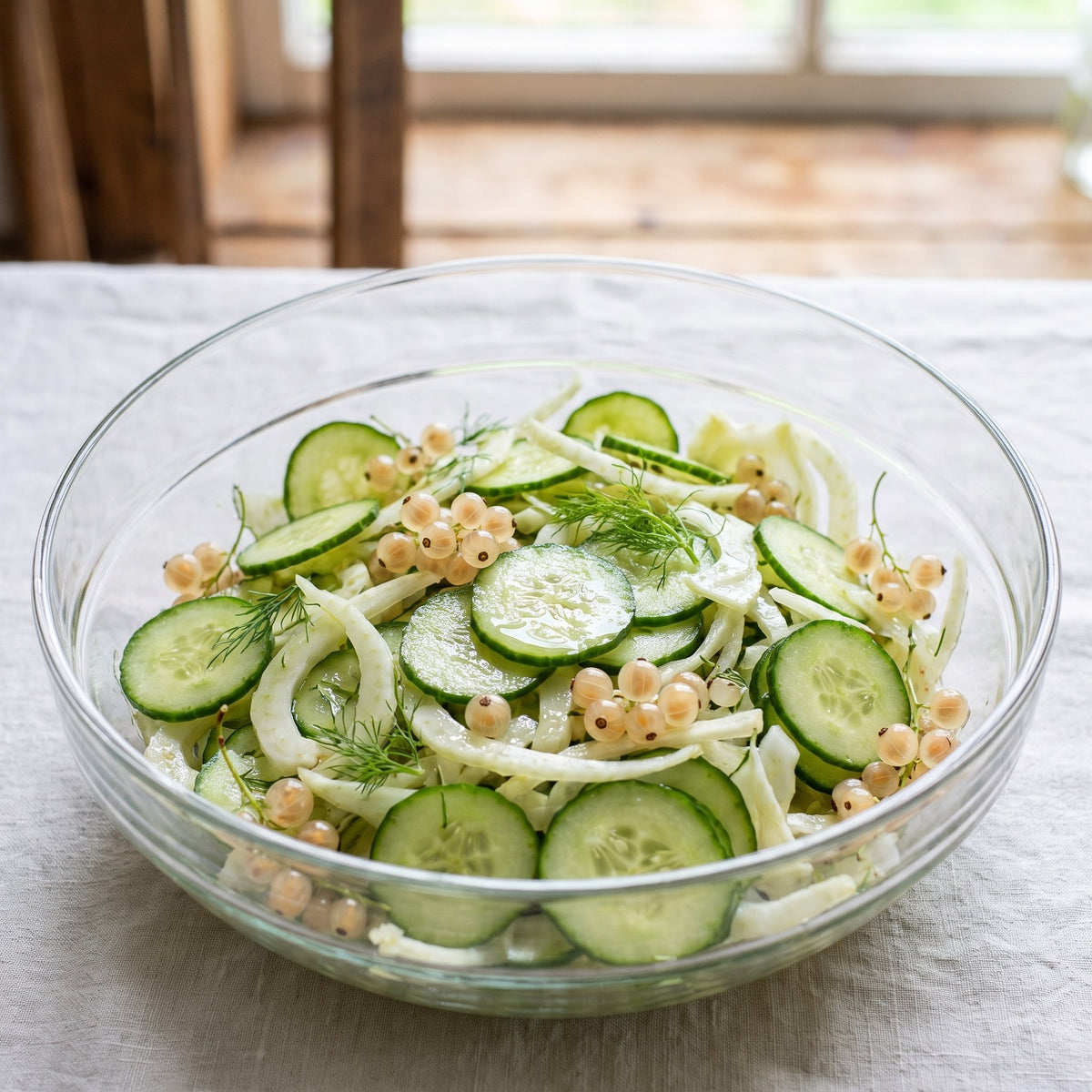 Salade de concombres en tranches avec fenouil, garnie de petites baies de gadelle blanche, servie dans un bol de verre
