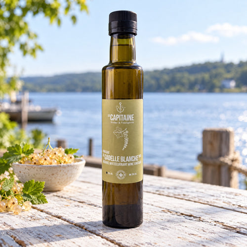 Bouteille de vinaigre gadelle blanche Le Capitaine sur une table de bois près d’un lac, avec bol de gadelles