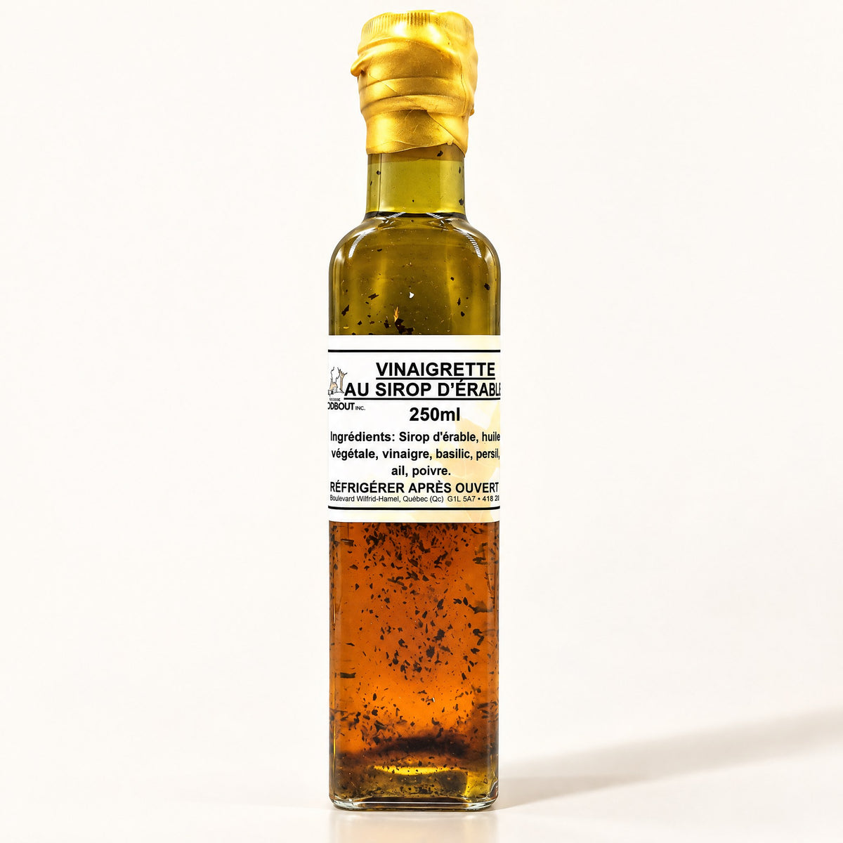 Bouteille de vinaigrette au sirop d’érable dressée seule sur fond crème, liquide ambré visible